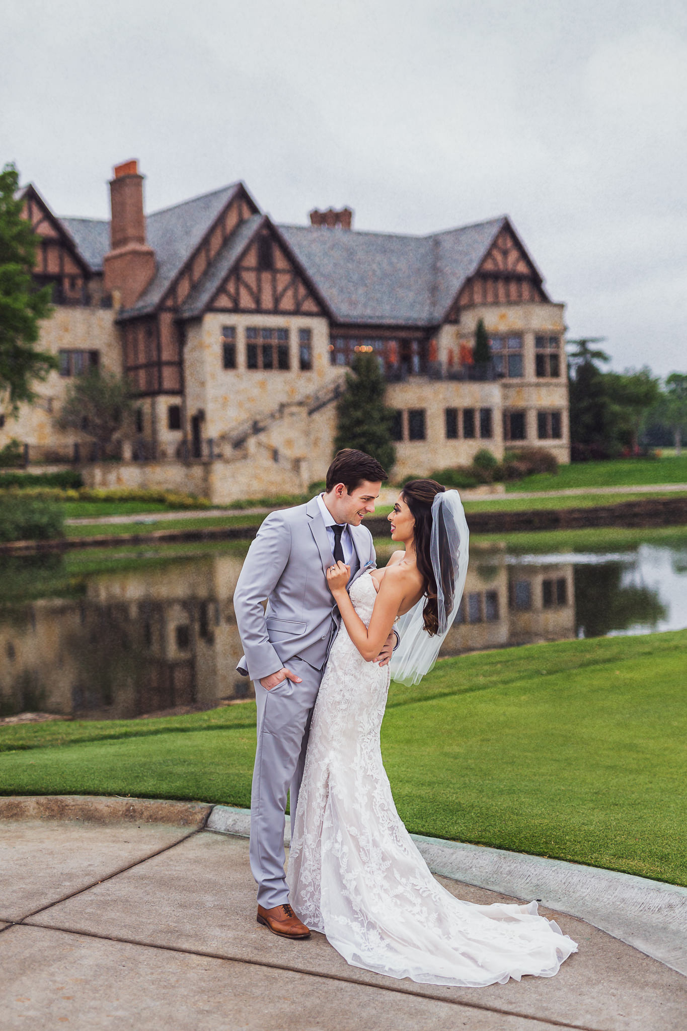 A couple is standing in front of a Dallas wedding venue estate. They are facing each other, and the groom has his hand on the bride's waist, dipping her slightly.